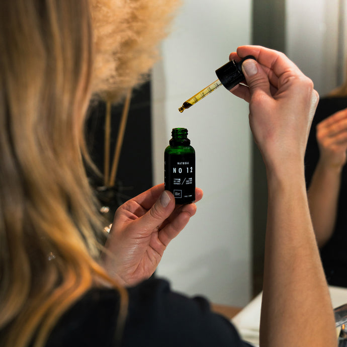 Kobieta używająca zakraplacza z butelki olejku CBD Eir Natural No. 12 przed lustrem, moment aplikacji produktu.