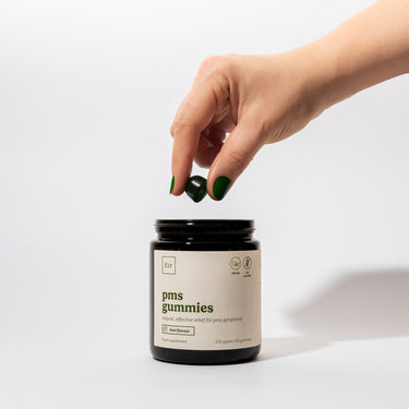 Dłoń z zielonym manicure trzymająca żelek na PMS nad czarnym słoikiem Eir Health, produkt wegański bez glutenu na dolegliwości menstruacyjne